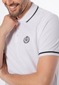 Bílá polokošile s černým lemováním a logem se "W" uvnitř vavřínového věnce na levé straně hrudi. Vyrobena z texturované tkaniny.