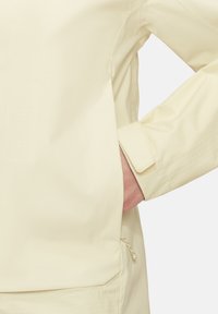 Gelbe Regenjacke mit glatter, glänzender Textur. Verfügt über einen karierten Bündchen und eine Seitentasche mit Kordelzug.