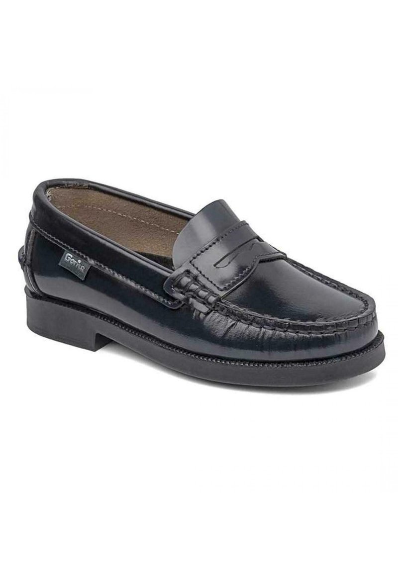 Mocasin de cuero negro con punta redondeada, costuras decorativas y un pequeño acento cosido en la parte frontal. Presenta un tacón bajo y una textura suave.