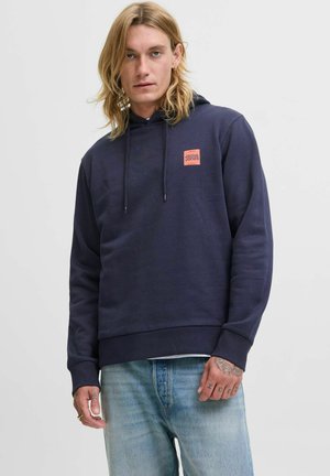 Navy blue hoodie with drawstrings, featuring a rectangular orange logo on the chest, and a relaxed fit. Paired with light blue jeans.