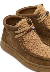 Brązowe zamszowe botki za kostkę z górną częścią z teksturowanej tkaniny w odcieniu tan, dekoracyjnym skórzanym sznurowaniem oraz kolorowymi drewnianymi koralikami na kołnierzu.