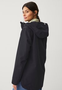 Zwarte waterdichte jas met capuchon, ritssluiting aan de voorkant en accentstiksel. Heeft een gladde, matte textuur en een langere achterzoom.