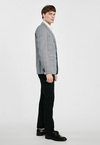 Szary marynarka w kratę z wyrazistymi klapami, zapinana na jeden guzik, w połączeniu z czarnymi spodniami i czarnymi eleganckimi butami. Gładki materiał, dopasowany krój.