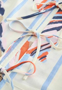 Material cu modele abstracte de tușe albastre, portocalii și roz, prezentând fundițe legate din benzi de pânză cu dungi asortate.