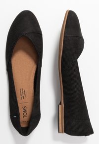 Černé slip-on boty TOMS s perforovaným textilním svrškem, zaoblenou špičkou, nízkým podpatkem a hnědou stélkou. Lehké a ploché provedení.