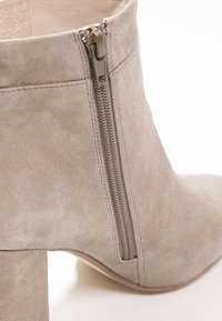 Stivaletto alla caviglia in suede grigia con tacco a blocco, cerniera laterale e interno liscio. La texture è morbida e il design è semplice e moderno.