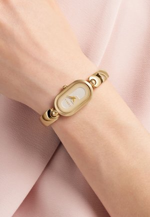 Montre bracelet dorée avec un boîtier ovale, un cadran blanc texturé et des marqueurs d'heure minimalistes, dotée d'un bracelet flexible et d'accents circulaires.