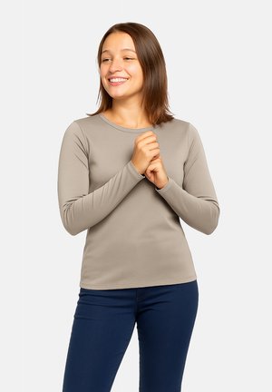 Maglietta a maniche lunghe e scollo rotondo di un colore taupe chiaro, realizzata in un tessuto morbido e elasticizzato; indossata con pantaloni blu scuro.