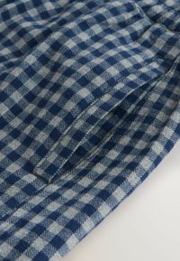 Sinine ja hall ruuduline kangas, mis on kaetud houndstooth mustriga, sujuva tekstuuriga ning küljetasku detailiga.