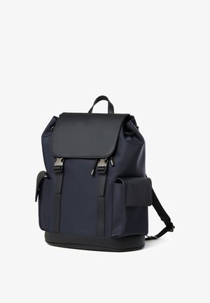 Marineblauer Rucksack mit schwarzer Klappe, Seitentaschen, Frontgurten mit silbernen Schnallen und einem oberen Tragegriff.