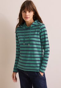 Maglietta a maniche lunghe con cappuccio, caratterizzata da strisce orizzontali verdi e blu scuro, con cordini regolabili e una vestibilità rilassata. Materiale in cotone morbido.