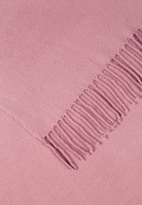 Tissu tricoté rose pâle avec une rangée de franges régulièrement espacées le long d'un bord, montrant une texture détaillée et un tissage de fibres.