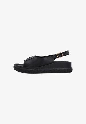 Black open-toe sandal with textured flat sole, slingback strap with gold buckle, and decorative circular detail on upper.