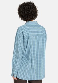 Langemouwige geruite overhemd in lichtblauw en groen. Voorzien van een knoopsluiting kraag, rugpand, en een relaxed fit met knoopmanchetten en geplooide details.