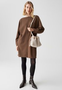 Bruine oversized gebreide jurk met een rechte snit, lange mouwen en een hoge halslijn. Gekocht met zwarte panty's en puntige enkellaarsjes.