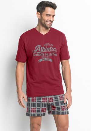 Rotes V-Ausschnitt-T-Shirt mit grauem Grafikdruck. Kombiniert mit karierten Shorts in Grau, Rot und Schwarz, die einen lockeren Schnitt und einen weichen Stoff haben.