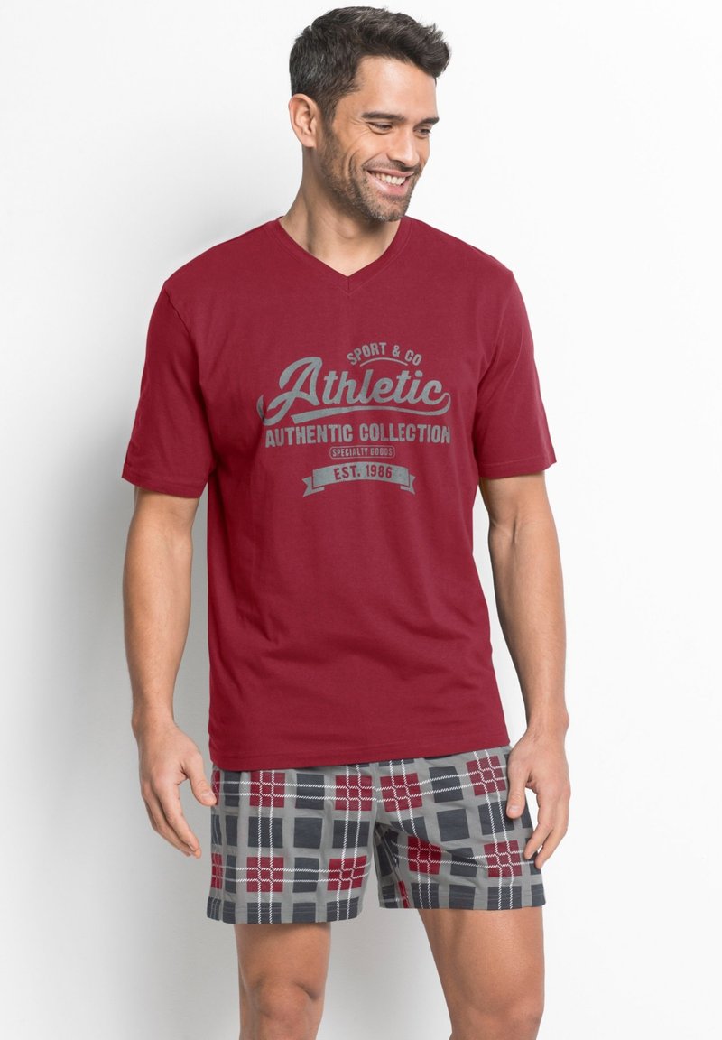 T-shirt rossa con scollo a V e stampa grafica grigia. Abbinata a pantaloni corti in plaid grigi, rossi e neri, con una vestibilità comoda e tessuto morbido.