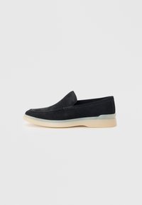 Svarte semskede slip-ons med rund tå, kontrasterende kremfarget såle og subtile stikninger. Enkel, minimalistisk design.