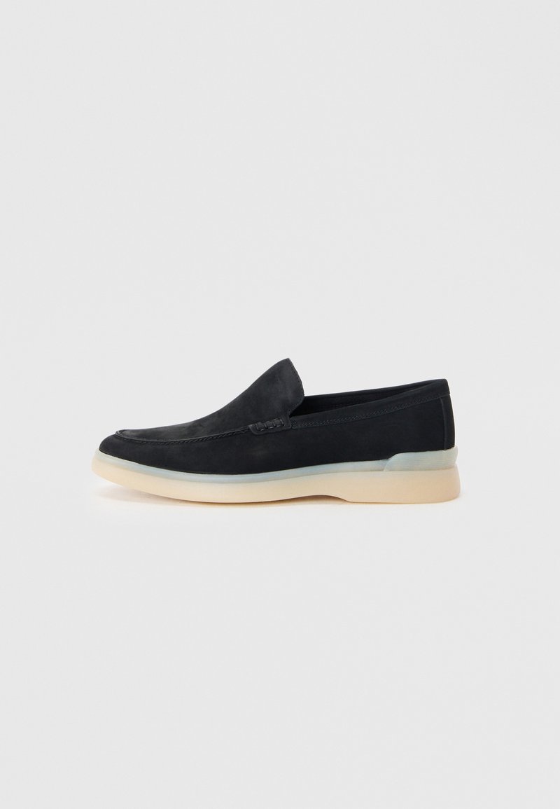 Svarte semskede slip-ons med rund tå, kontrasterende kremfarget såle og subtile stikninger. Enkel, minimalistisk design.