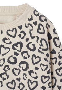 Beige Stoff mit schwarzem Herz und abstraktem Leopardenmuster sowie geripptem Rundhalsausschnitt.