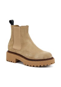 Bota Chelsea de ante beige con paneles laterales elásticos, punta redondeada y suela de goma gruesa y estriada. Cuenta con una tira en la parte posterior.