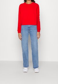 Czerwony krótki sweatshirt z rękawami raglanowymi, w zestawie z jasnoniebieskimi spodniami dżinsowymi o prostym kroju i białymi sneakersami. Minimalistyczny design i miękka tekstura.