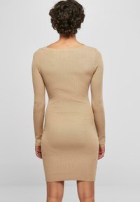 Robe à manches longues à côtes de couleur beige, silhouette ajustée, longueur genou, avec un décolleté arrondi dans le dos et un tissu texturé.