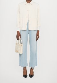 Jasno beżowa kurtka zapinana na guziki, jasnoniebieskie szerokie dżinsy z postrzępionymi brzegami, biała torebka oraz czarne szpilki.