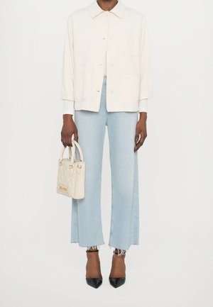 Giacca button-up beige chiaro, jeans a gamba larga blu chiaro con orli sfrangiati, borsa bianca e tacchi a punta neri.