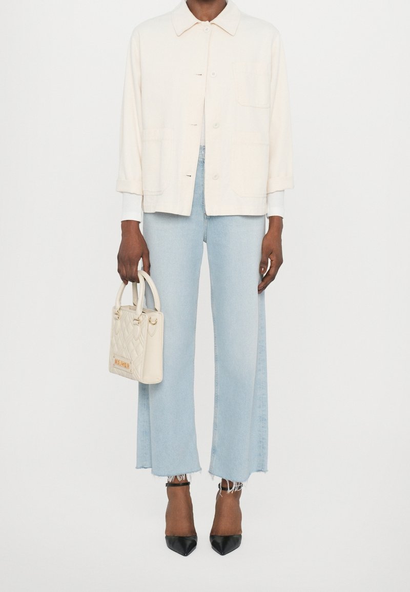 Jasno beżowa kurtka zapinana na guziki, jasnoniebieskie szerokie dżinsy z postrzępionymi brzegami, biała torebka oraz czarne szpilki.