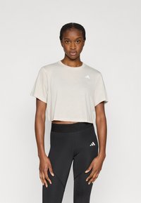 Κοντοκομμένο μπεζ μπλουζάκι από ελαφρύ υλικό, με στρογγυλή λαιμόκοψη και κοντά μανίκια. Συνδυάζεται με μαύρα ψηλόμεσα κολάν με διακοσμητικές λεπτομέρειες.