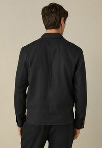 Black casual jacket, textured fabric, standard collar, buttoned cuffs, and back seam detail. Worn with matching pants.