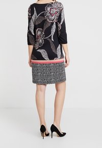 Haut noir avec imprimé floral et manches trois-quarts, associé à une jupe à motifs noir et blanc. Modèle portant des talons hauts noirs.