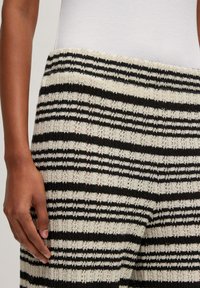 Gestreifte Strickhose in Schwarz und Elfenbein mit strukturierter Oberfläche. Der Bund ist elastisch und der Stoff weist ein dezentes offenes Gewebemuster auf.