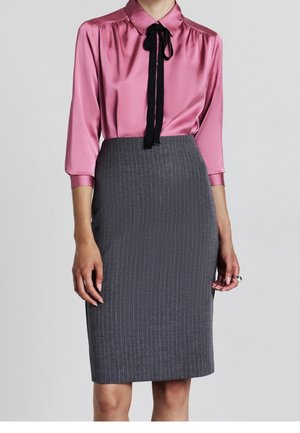 Femme portant un chemisier en satin rose avec une cravate noire et une jupe crayon grise à rayures taille haute.
