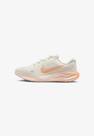 Chaussure de course Nike beige clair et pêche avec tige en mesh, semelle amortie et fermeture à lacets, montrée de profil face à gauche.
