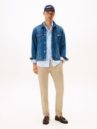 Denim jacket, light blue striped shirt, khaki trousers, black loafers, and a navy cap with a red and white stripe detail.