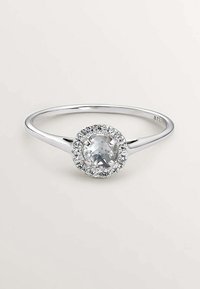 Anillo de plata con una piedra central redonda y clara, rodeada de un halo de piedras más pequeñas y claras en una banda delgada.