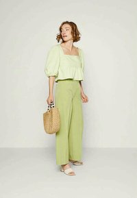 Top verde claro de mangas bufantes, decote quadrado, design em camadas, combinado com calças largas verde claro, bolsa bege trançada e sandálias brancas.