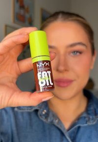 NYX Fat Oil in een doorzichtige fles met een groene dop. Het etiket heeft vetgedrukte witte en groene tekst. Maat: 0,16 fl. oz. of 4,8 mL.