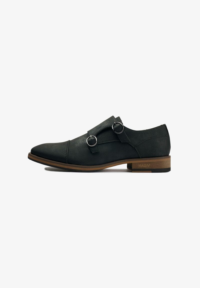 Black leather shoe with a smooth texture, pointed toe, and two metal buckle accents. Features a brown wooden heel and minimal branding.