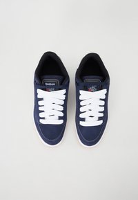Blue sneakers with white laces, featuring a smooth fabric upper, padded collar, and a rubber outsole. Logo on the tongue.