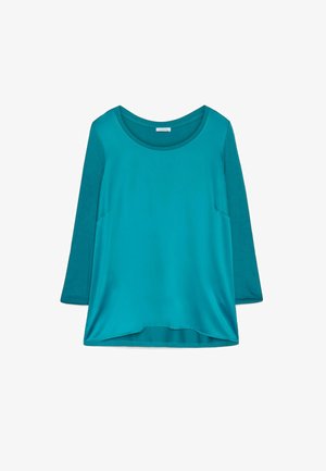 Bluză lungă cu mâneci, de culoare verde-albăstrie, cu decolteu rotund. Textură moale, croială lejeră și mâneci contrastante. Fără modele sau accesorii proeminente.