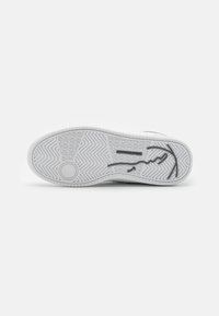 Hvit sneakersåle med teksturert gummi, mønstret dekk og en formet logo preget på bunnen. Glatte kanter og sirkulært grep.