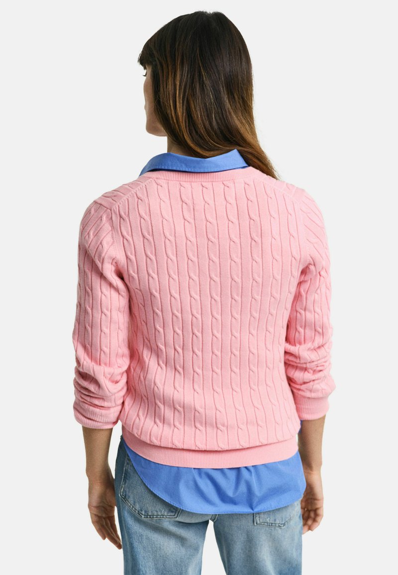 Suéter de punto rosa con mangas largas y puños acanalados, superpuesto a una camisa de cuello azul, visto desde atrás.
