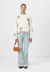 Cream sweatshirt with sun embroidery, light blue flared jeans, black shoes, and a small brown handbag. Simple design and casual fit.