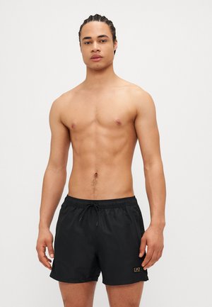 Black swim shorts with an elastic waistband and drawstring. Features a subtle EA7 logo in gold. Material appears lightweight and textured.