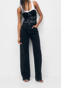 Jeans de pernera ancha negros combinados con un corsé de encaje negro y una camiseta sin mangas blanca, con una textura suave y un diseño ajustado.