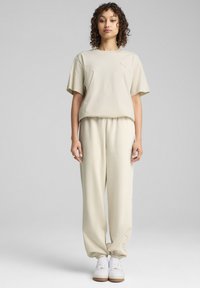 Beige cotton T-shirt with short sleeves and a small logo, paired with matching tapered jogger pants. Both have a soft texture.