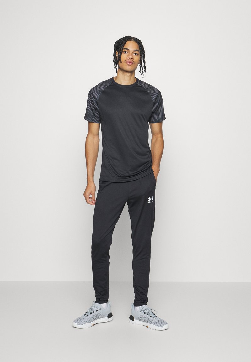 Czarny sportowy t-shirt z fakturowanymi rękawami, w połączeniu z czarnymi spodniami i szarymi butami do biegania z wzorzystymi akcentami z siateczki.